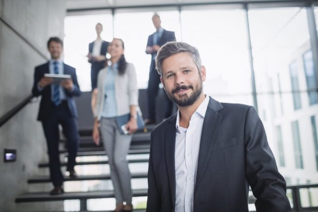 Photo of businessman with employees illustrates blog: "Taking Your Hiring to the Next Level in 2022"