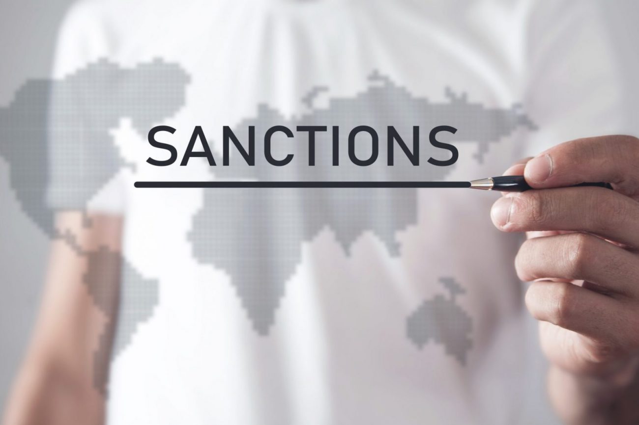 Photo of man writing the word "Sanctions" on a translucent map illustratees blog: "What Are OFAC Sanctions?"