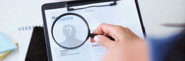 Photo of hand holding magnifying glass over resume illustrates blog: "Are Background Checks Accurate?"