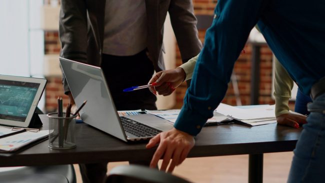 Photo of three people looking at laptop illustrates blog:; "How Long Does It Take To Complete a Background Check?"