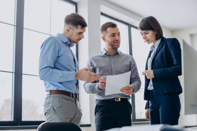 Three executives talking holding sheets of paper.