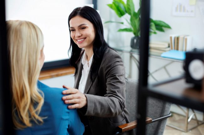 Woman with her hand on the shoulder of another woman seen from behind illustrates blog "What Is Skills-First Hiring?"