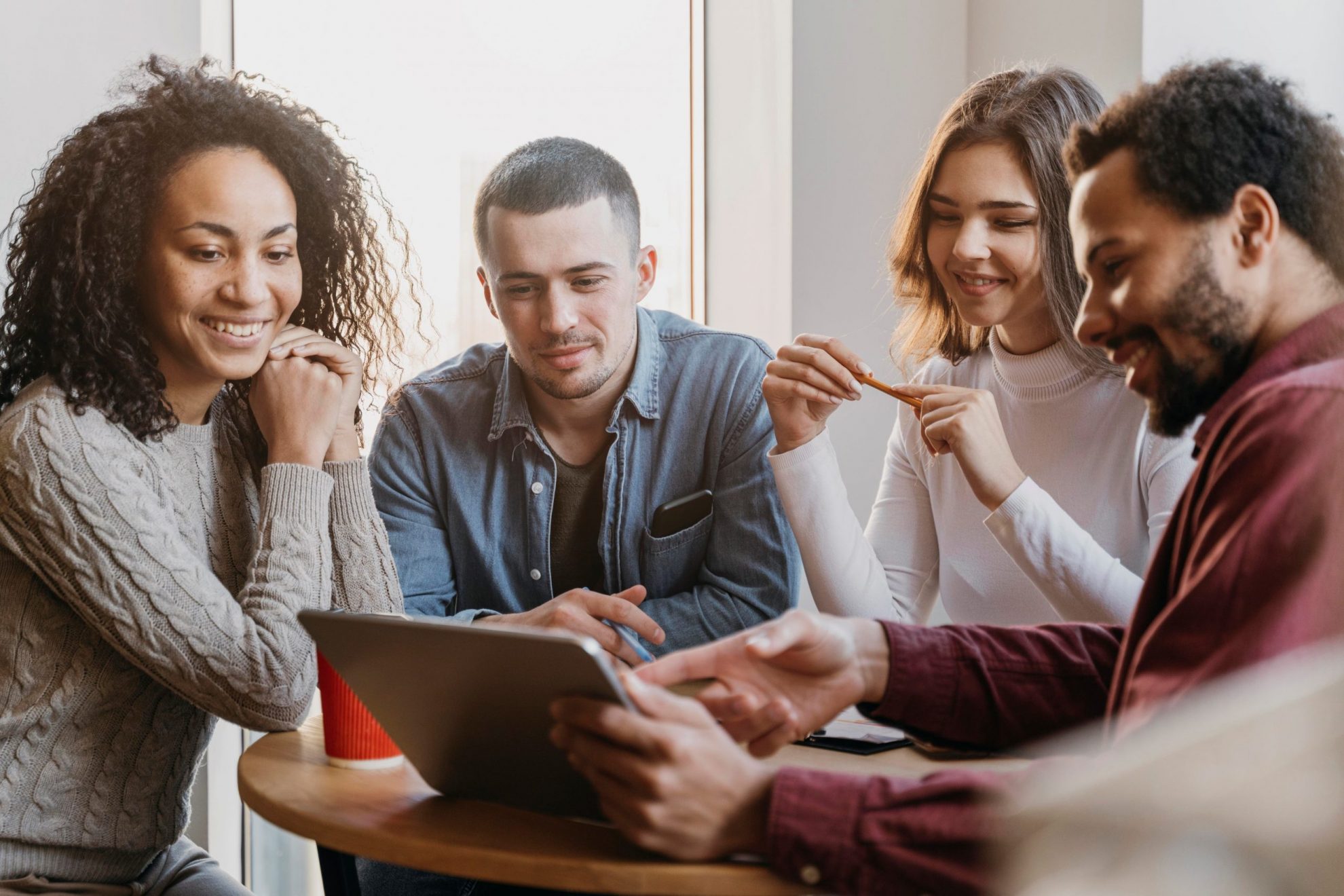 Group of four people looking at tablet illustrates blog "How To Build a Strong Company Culture"