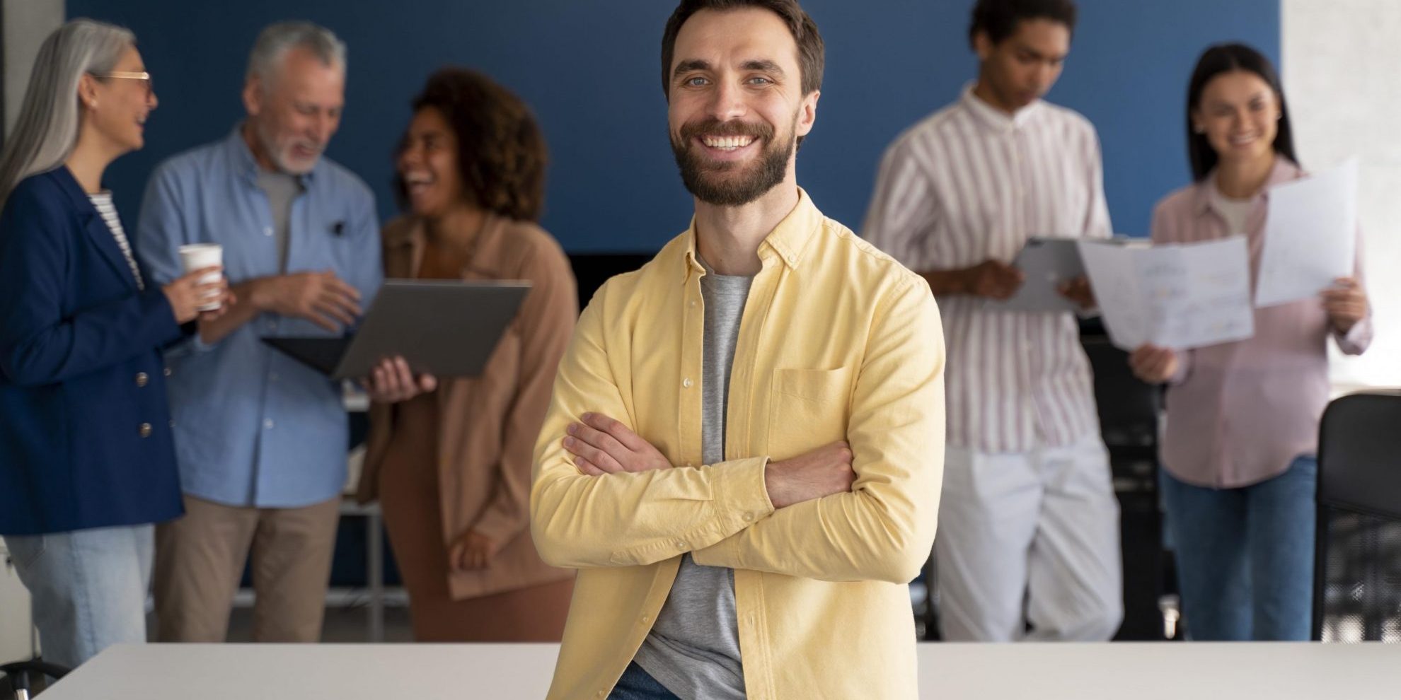 employer-employee-fp Man sitting on desk with people in the background illustrates blog "When To Run Background Checks?"