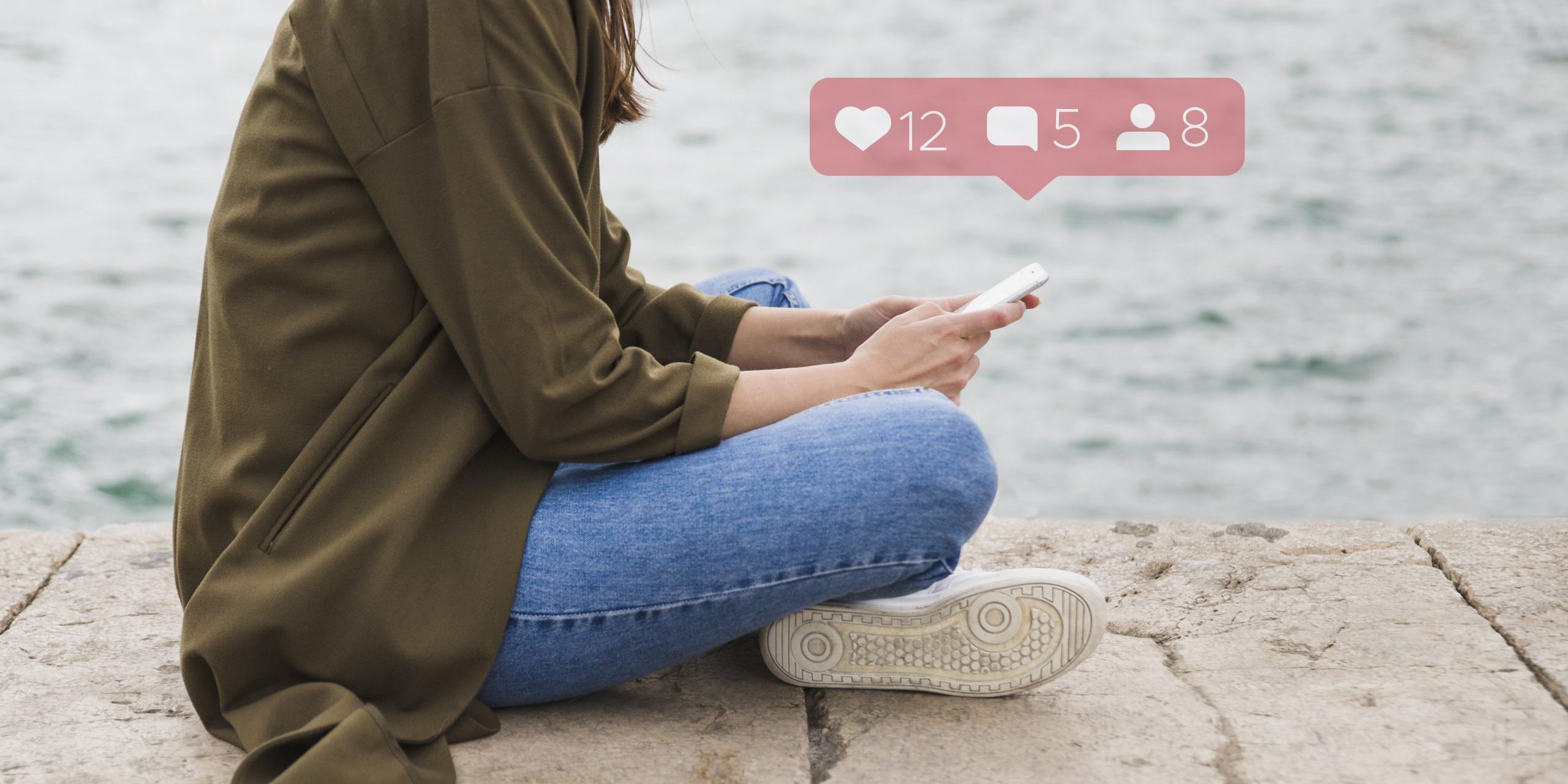 social-media-fp Woman wearing jeans and a green jacket sitting on the floor holding smartphone with social media icons hovering above it.