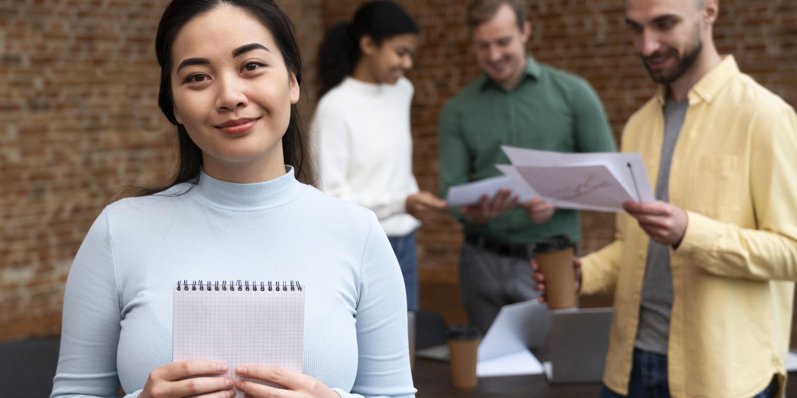job-candidates-fp Woman holding notebook with people in the background in office.