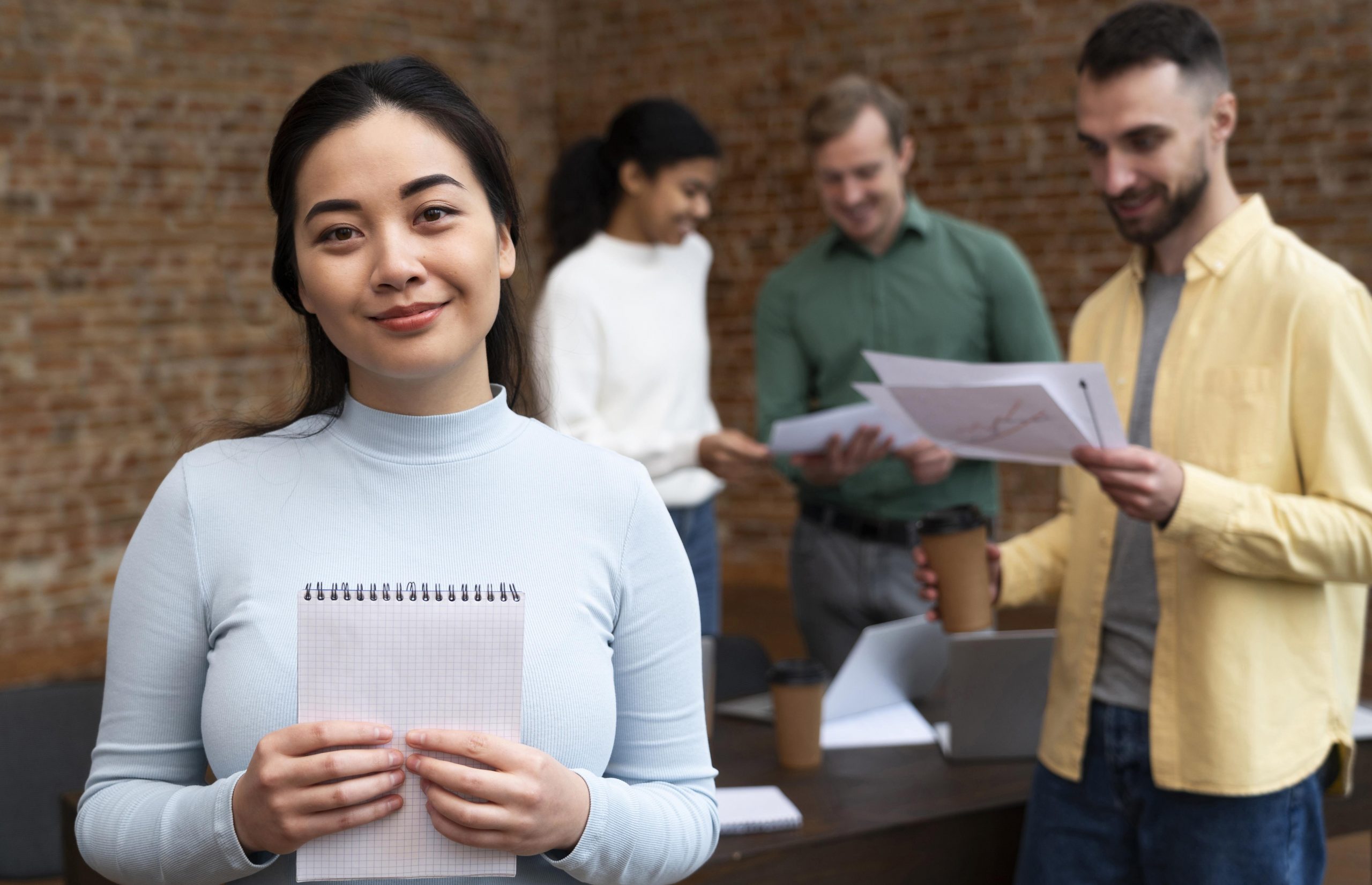 Woman holding notebook with people in the background in office.