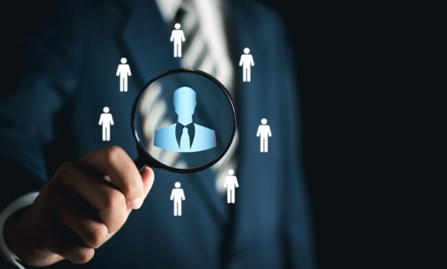 Businessman using magnifying glass to look at personnel icon on virtual social network interface. Personal network structure. Concepts of human resource management and recruitment.
